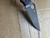 Used Spyderco Military 2 Salt folding knife with thumb hole - close up of presentation side blade shown.  Black CPM MagnaCut stainless steel plain edge blade.  Black G-10 handle.  Model C36GMCBKP2.