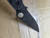 Used Spyderco Military 2 Salt folding knife with thumb hole - close up of pocket clip side blade shown.  Black CPM MagnaCut stainless steel plain edge blade.  Black G-10 handle.  Model C36GMCBKP2.