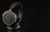 Audeze MM-100 resting on dark reflective surface, angled front grille view with Manny Marroquin text and Audeze logo on headband