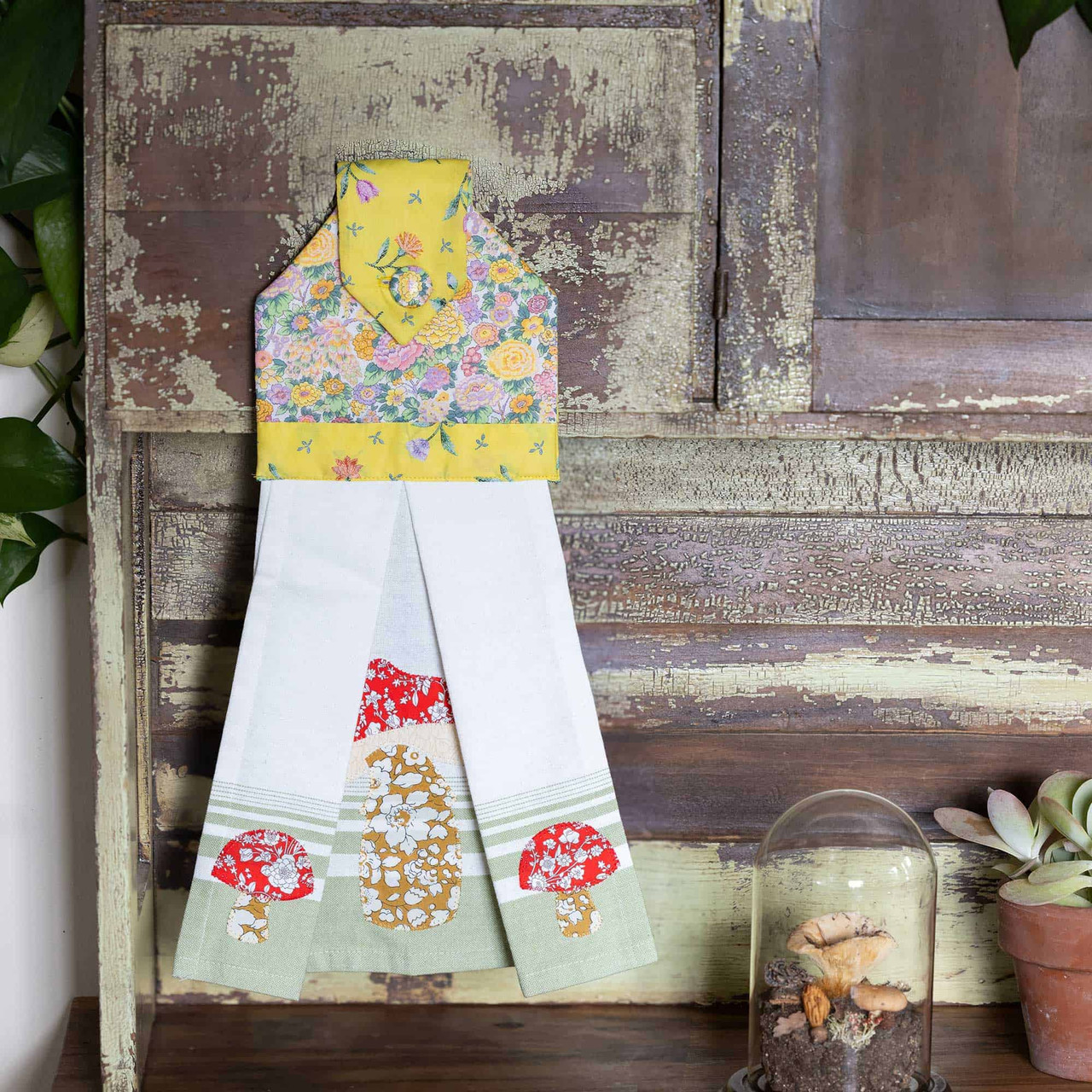 Colorful fabric towel with floral and mushroom patterns hanging on a rustic shelf.