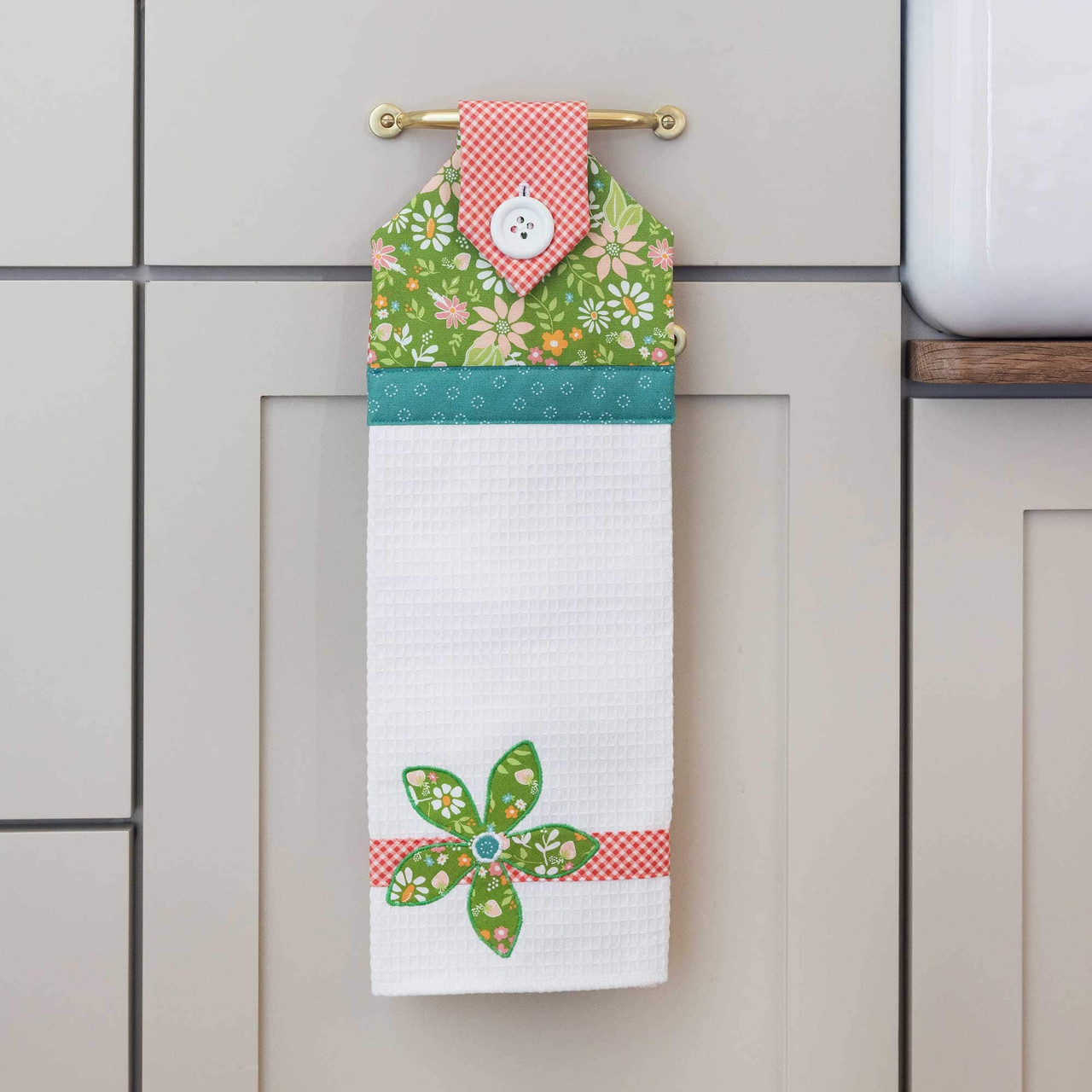 Colorful fabric hand towel with floral patterns hangs on a kitchen cabinet handle.