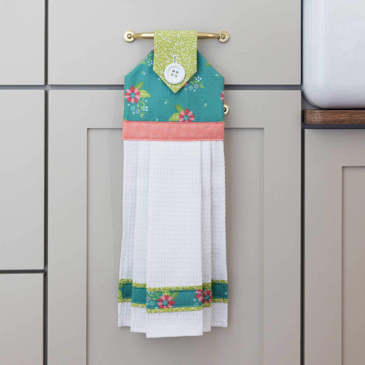 Hanging fabric towel with colorful floral trim on a brass kitchen handle.