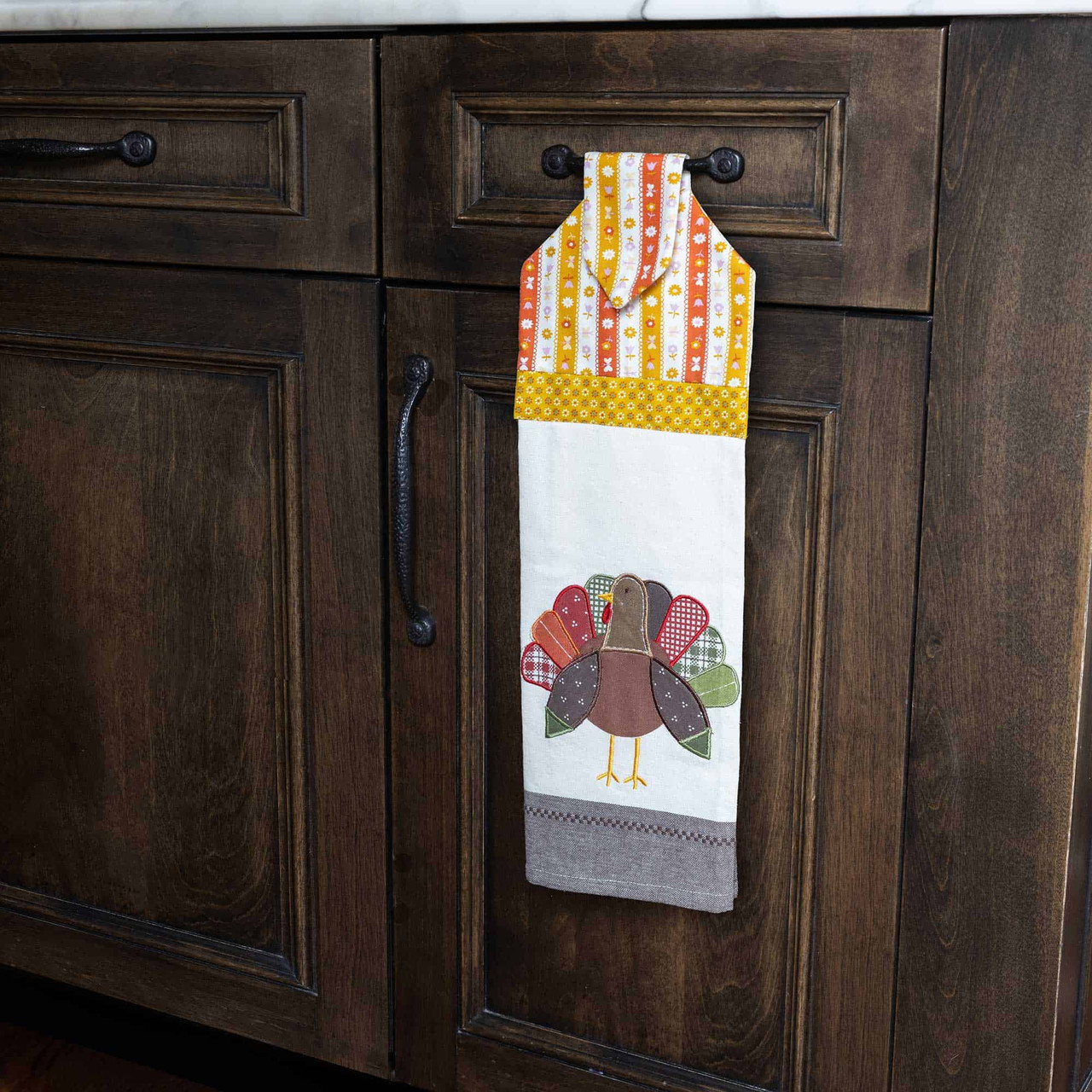 Kitchen towel with a turkey design hangs on a wooden cabinet handle.