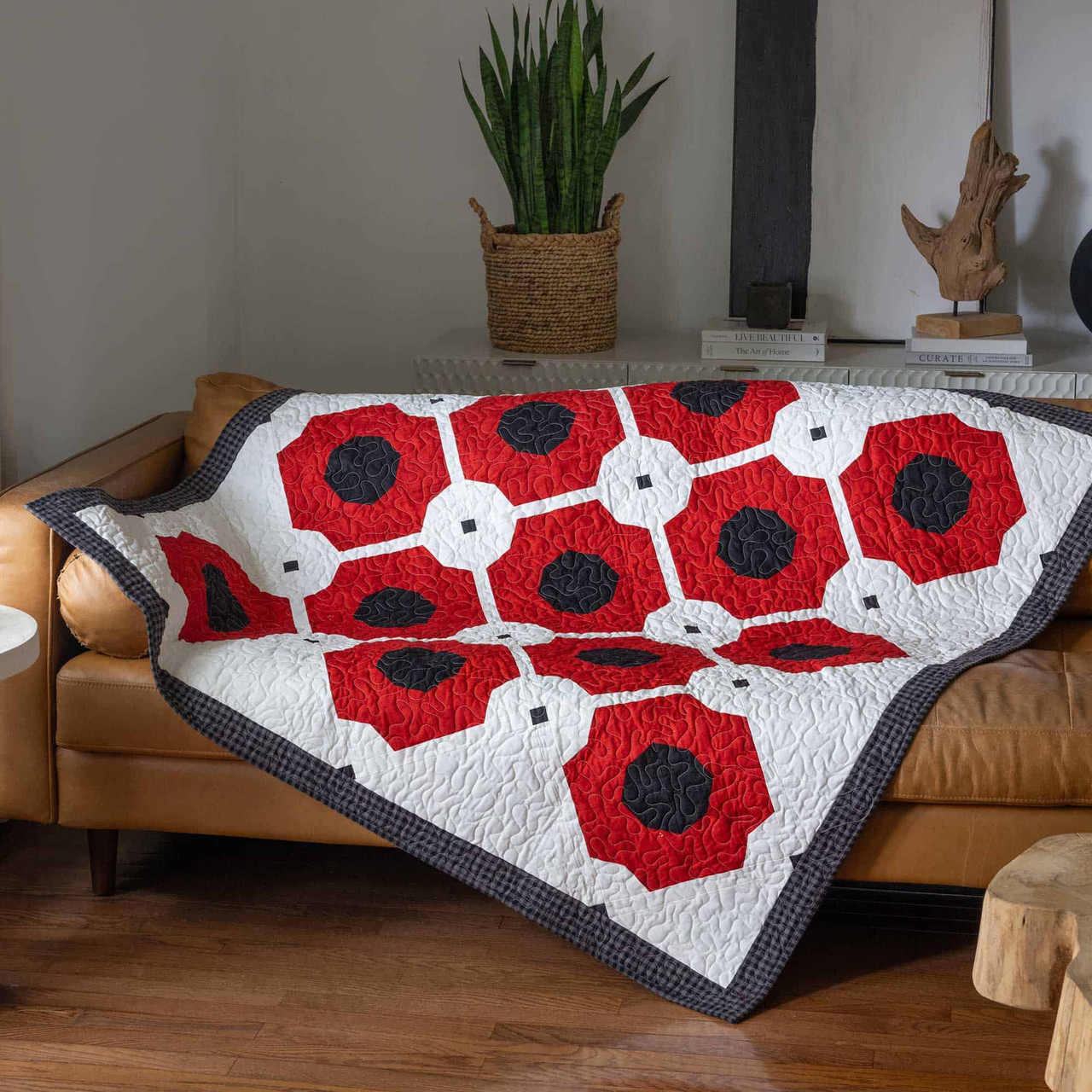 A vibrant red and white quilt drapes over a cozy brown leather sofa.