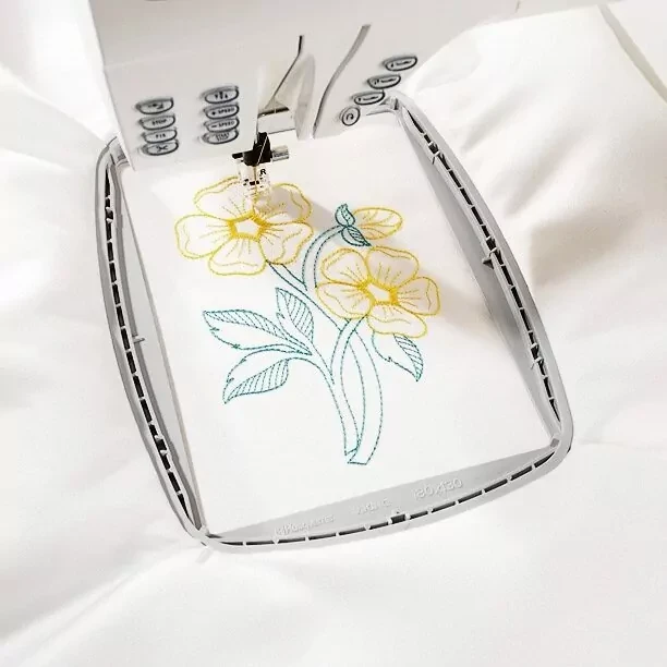 Sewing machine embroidering yellow and blue flowers on white fabric.