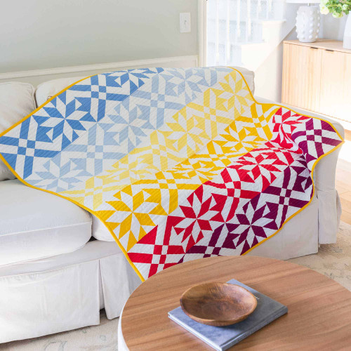 Colorful geometric quilt draped over a white sofa in a bright living room.