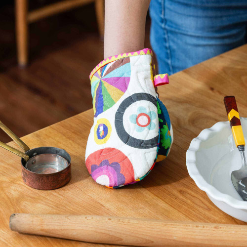 Colorful oven mitt on wooden table with baking tools nearby.