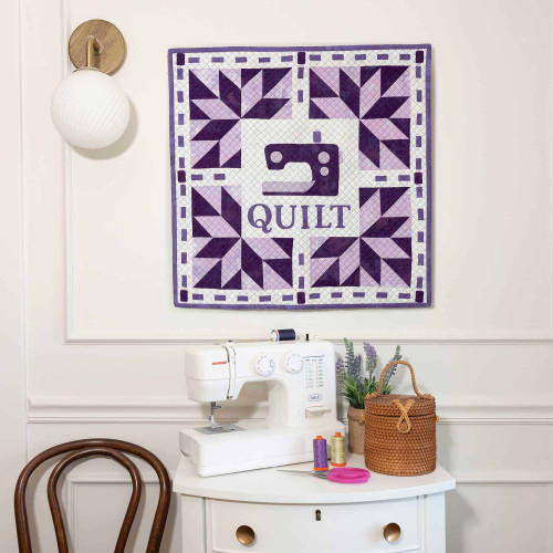 Sewing station with a quilted wall hanging and fabric cutter tools displayed.