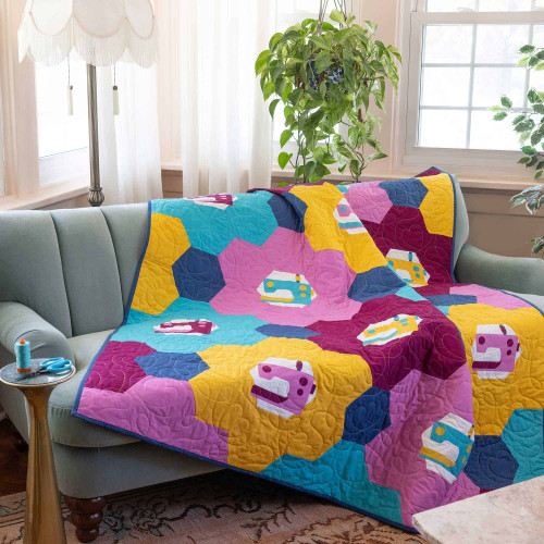 Colorful quilt with sewing machine patterns draped over a couch.