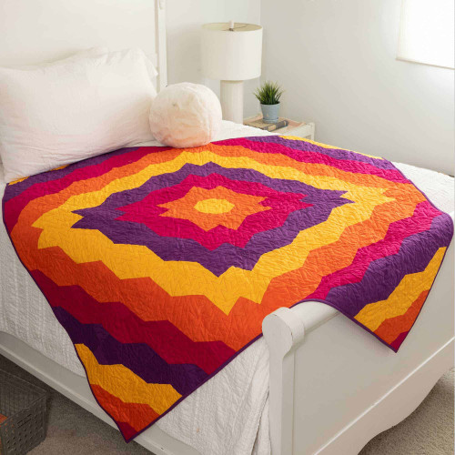 Colorful geometric quilt on a white bed in a bright modern bedroom.