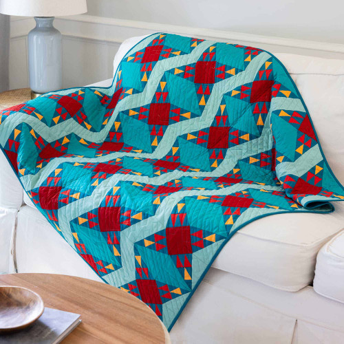 Colorful geometric quilt draped over a white sofa in a cozy living room.