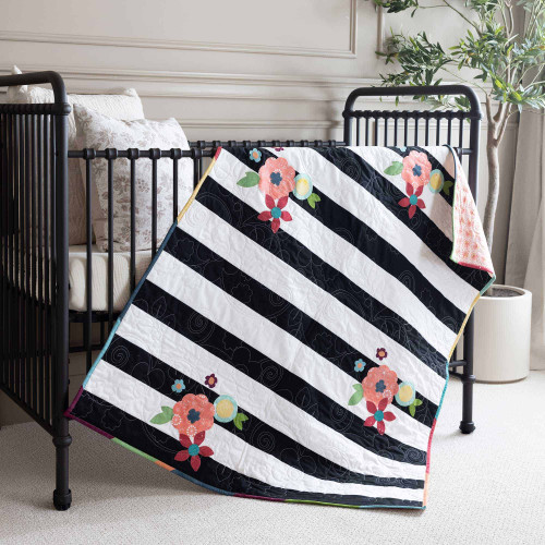 Quilt with floral patterns draped over a crib in a cozy nursery setting.