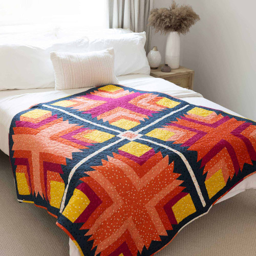 Vibrant handmade quilt with geometric patterns on a white bed in a cozy room.