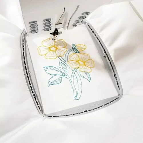 Sewing machine embroidering yellow and blue flowers on white fabric.
