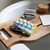Colorful towel and grooming items on a wooden tray over a bathtub edge.
