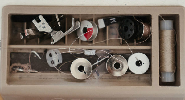 a small collection of sewing essentials including sewing machine feet, bobbins, and thread