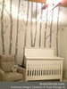 Gray birch tree wall decals installed in a neutral nursery with white crib, glider chair, and woodland wall decor