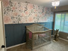 Olivia Rose Watercolor Wallpaper installed in a nursery with blue green wall paneling, white crib, window light, and oversized pink floral wallpaper