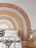 Oversized terracotta rainbow wall decal displayed behind a rattan bed with neutral striped bedding