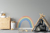 Small pastel watercolor rainbow wall decal displayed in a neutral playroom beside a wood dresser and black play tent