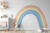 Oversized watercolor rainbow wall decal in a bright children’s room with white furniture and colorful toys