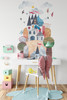 Tall pink castle mountain wall decal with village, windmill and rainbow displayed above a white crib in a nursery alcove