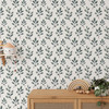 Fergus blue green botanical wallpaper styled above a natural wood dresser with soft watercolor foliage and light neutral decor