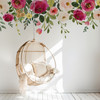 Vintage floral wall decal border with pink roses, burgundy flowers and greenery installed above a hanging rattan chair in a girls room.