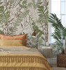 Green and brown foliage wallpaper in a warm bedroom with ochre bedding and natural woven decor