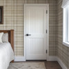 Neutral beige plaid wallpaper in 26 inch repeat styled in a cozy bedroom with white paneled door, wood bed, and farmhouse cottage decor
