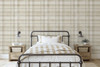 Neutral beige plaid wallpaper in 52 inch repeat styled in a farmhouse bedroom with black metal bed, wood nightstands, wall sconces, and beige bedding