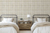 Neutral beige plaid wallpaper in 26 inch repeat styled in a farmhouse bedroom with twin beds, black metal headboards, wood nightstand, and cream bedding