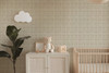 Neutral beige plaid wallpaper in 13 inch repeat styled in a soft nursery with crib, teddy bear, storage cabinet, plant, and cloud wall decor