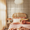 Neutral beige plaid wallpaper in 52 inch repeat styled in a warm girls bedroom with rattan headboard, peach bedding, paper pendant light, and boho cottage decor