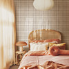 Neutral beige plaid wallpaper in 26 inch repeat styled in a warm girls bedroom with rattan headboard, peach bedding, paper pendant light, and boho cottage decor