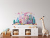 Small fairytale castle wall decal displayed above white storage furniture in a child’s room with a giraffe toy