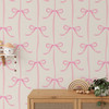 Pink bows nursery wallpaper with smaller ribbon pattern behind a wood cabinet and children’s decorations