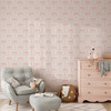 Pastel pink bow wallpaper with delicate repeating ribbons in a neutral nursery with gray chair and blush dresser