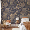 Midnight Botanica navy and antique gold floral wallpaper in a bedroom with a grey upholstered bed and rattan chair, shown in the 78-inch repeat