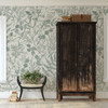 Vintage wooden armoire displayed against Rosemary Botanical Wallpaper with botanical fern pattern.