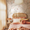 Magnolia Chinoiserie Wallpaper styled in a peach bedroom with rattan headboard, soft bedding, warm curtains, and romantic floral branch wall decor