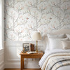 Magnolia Chinoiserie Wallpaper styled in a bright bedroom with white bedding, wood nightstand, table lamp, butterflies, and soft magnolia branch wallpaper