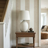 Neutral beige linen stripe wallpaper in an entryway with a wood console table and white lamp