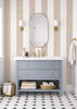 Beige and cream striped bathroom wallpaper with a gray vanity, oval mirror and brass sconces