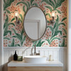 Green botanical wallpaper with coral flowers in a bathroom vanity with oval mirror and wall sconces