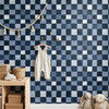 Blue checkered wallpaper in a nursery or kids room with white beadboard, brass hooks, and baby clothes