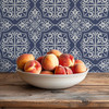 Blue fleur-de-lis tile wallpaper in 13-inch pattern scale with a bowl of peaches on a rustic table