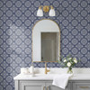 Navy fleur-de-lis tile wallpaper in 13-inch repeat in a bathroom with arched mirror, brass light, and white vanity