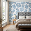 Blue watercolor floral wallpaper in a bedroom with upholstered bed, soft window light, and Scandinavian-inspired decor