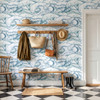 Marina blue Atlantic wave wallpaper in 52 inch repeat styled in a rustic entryway with wood hooks, woven bags, bench, boots, and coastal cottage decor